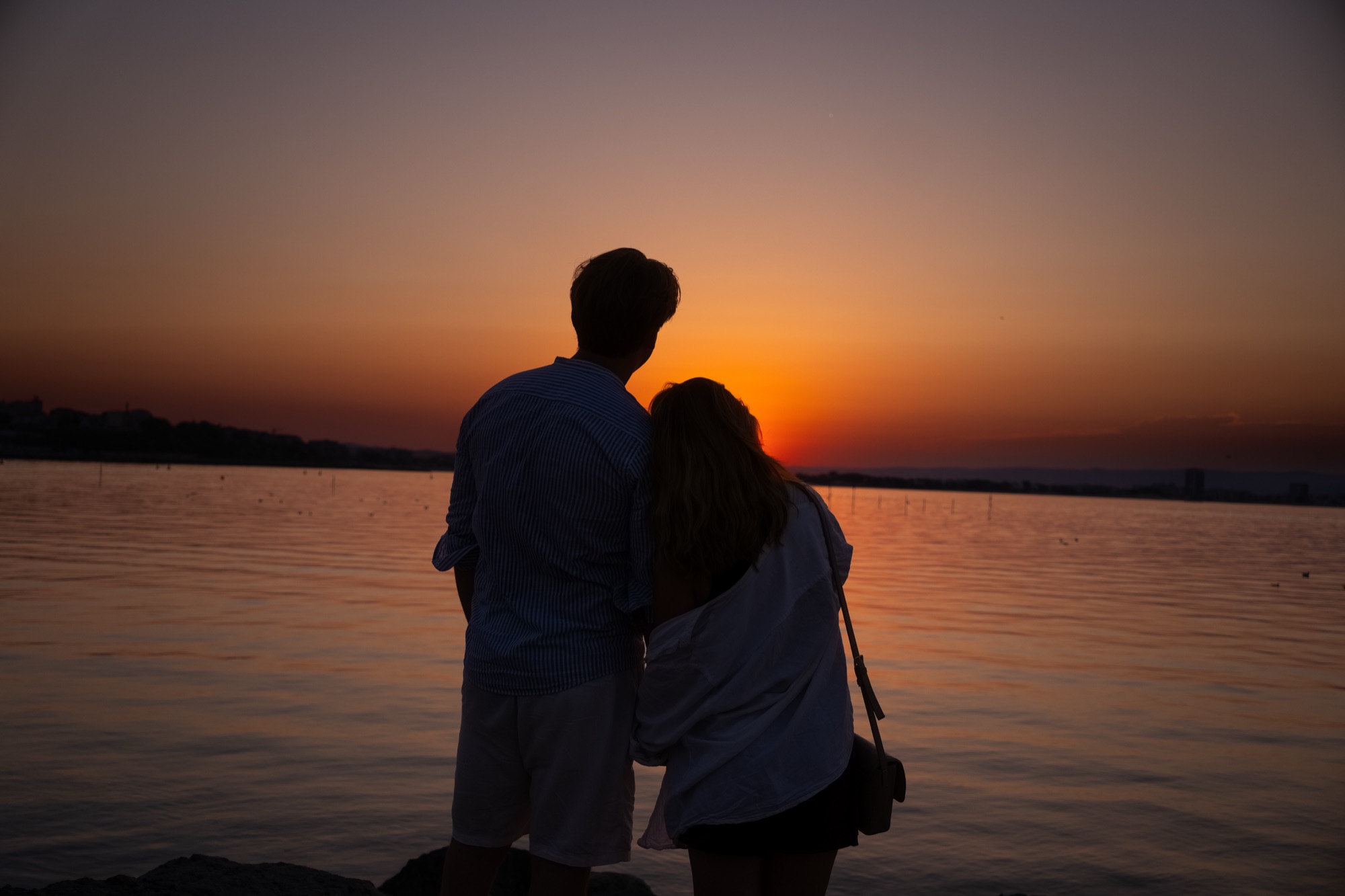 Koppel dat hand in hand naar de zonsondergang boven het water kijkt